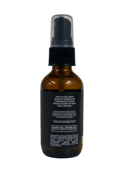 An amber glass spray bottle with a black spray top and a black label containing white text, photographed against a neutral light gray background.