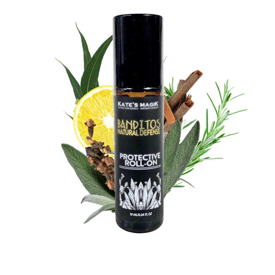 A black cylindrical roll-on bottle labeled 'Kate's Magic Banditos Natural Defense Protective Roll-On' centered on a white background, surrounded by botanical and spice props including sage leaves, a sliced lemon, cinnamon sticks, and cloves.