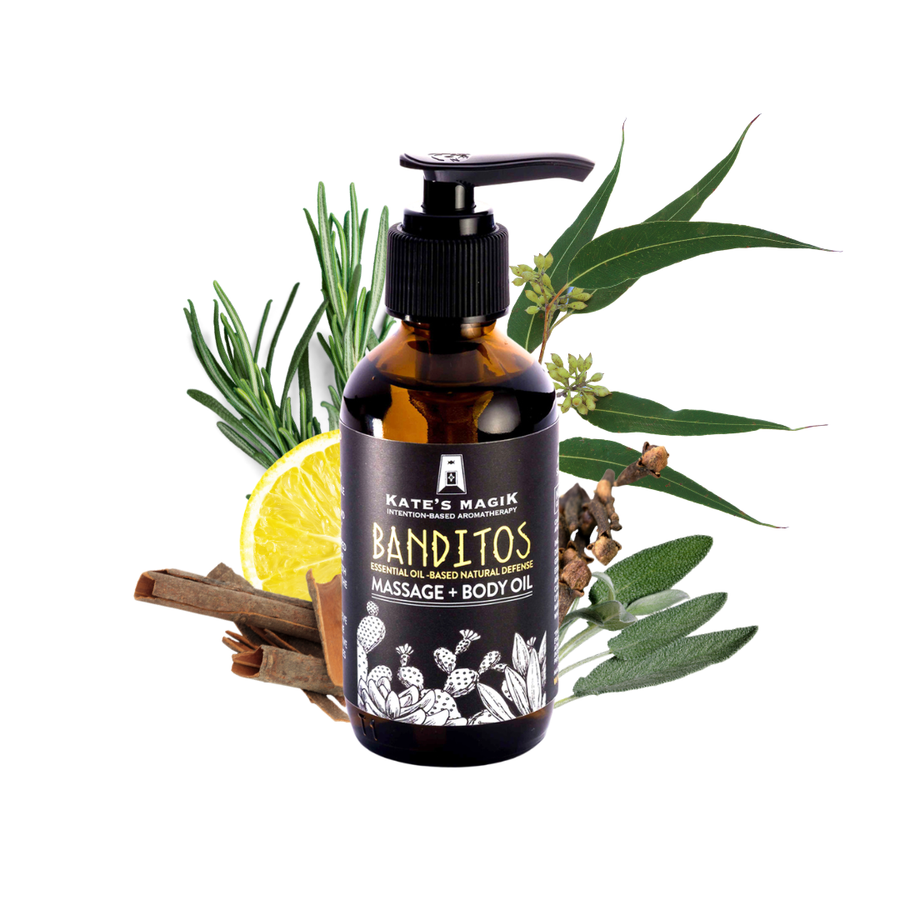A bottle of Kate's Magik Banditos Massage + Body Oil centered on a white background, surrounded by botanical ingredients including rosemary, eucalyptus leaves, cinnamon sticks, a lemon slice, and dried herbs.