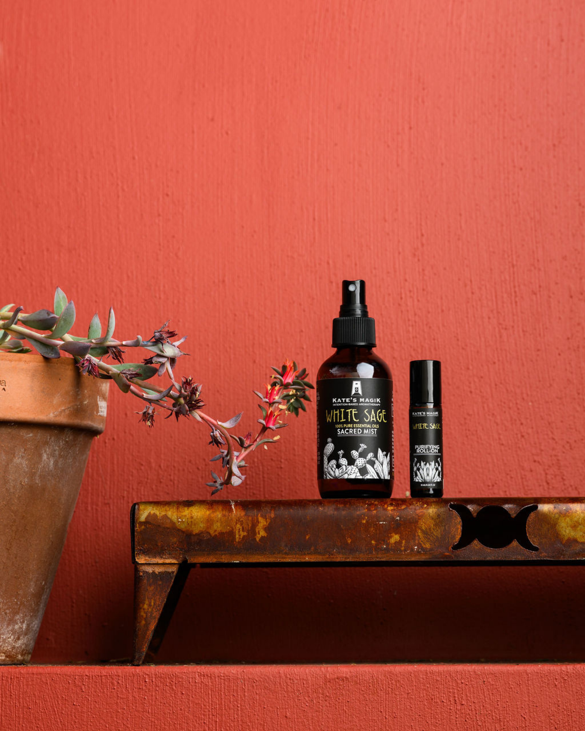 Two bottles of Kate's Magik White Sage aromatherapy products, including a larger White Sage Protective spray bottle and a smaller White Sage Purifying Roll-on, displayed on a rustic wooden shelf against a textured terracotta background.