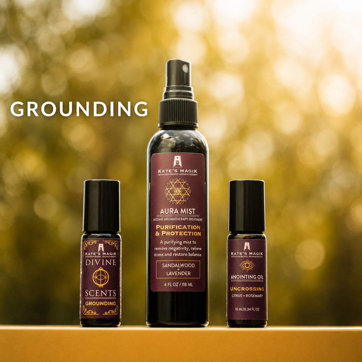 Three Kate's Magick essential oil and aromatherapy products displayed on a wooden surface against a blurred golden background: a Divine Scent grounding roll-on, a tall Aura Mist Purification & Protection bottle, and an Uncrossing Anointing Oil roll-on.